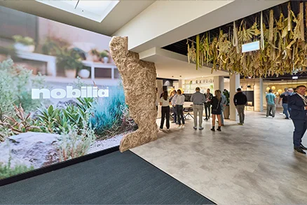 Besucher in der nobilia Ausstellung mit großem Markenmotiv und modernen Präsentationsflächen als Teaser für inspirierende Küchen, Bad und Wohnideen vor Ort.