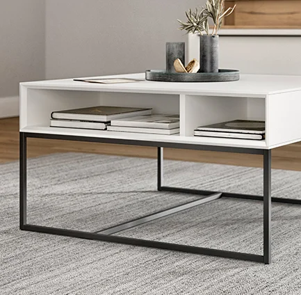 Minimalistyczny biały stolik kawowy z eleganckimi czarnymi metalowymi nogami, z otwartą półką na książki i dekoracje, w nowoczesnej przestrzeni dziennego wypoczynku.