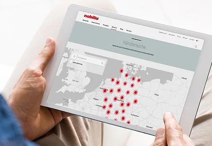 Persona che tiene un tablet con la ricerca rivenditori Nobilia aperta e una mappa piena di indicatori di posizione.