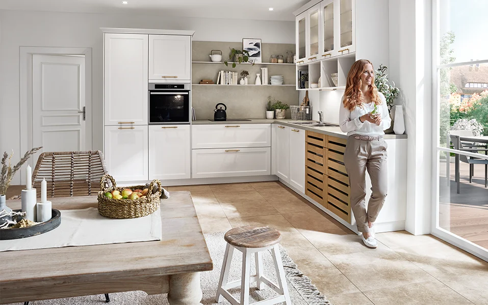 Lichtgekleurde landhuiskeuken met CASCADA 774 front in wit, gecombineerd met houten details en gouden handgrepen, open ontwerp met veel daglicht.