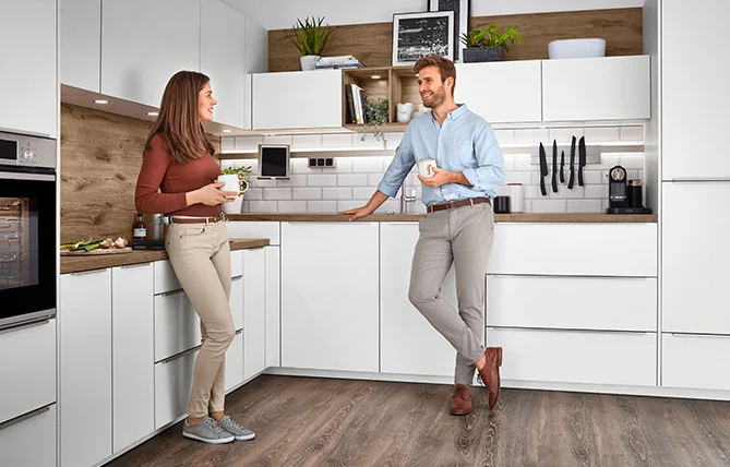 Une femme dans une cuisine moderne charge le lave-vaisselle, mettant en valeur les appareils intégrés élégants et la décoration minimaliste dans un espace lumineux et aéré.