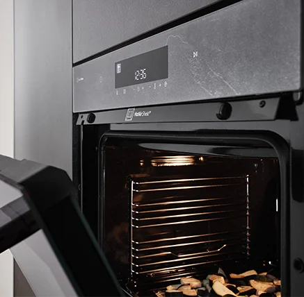[Translate to cs:] Laurus Backofen in Grauschiefer Nachbildung passend zur Küchenfront Stoneart 303 geöffnet mit aktivem HotAirShield und weißer Displayanzeige für moderne Backtechnologie in harmonischem Design