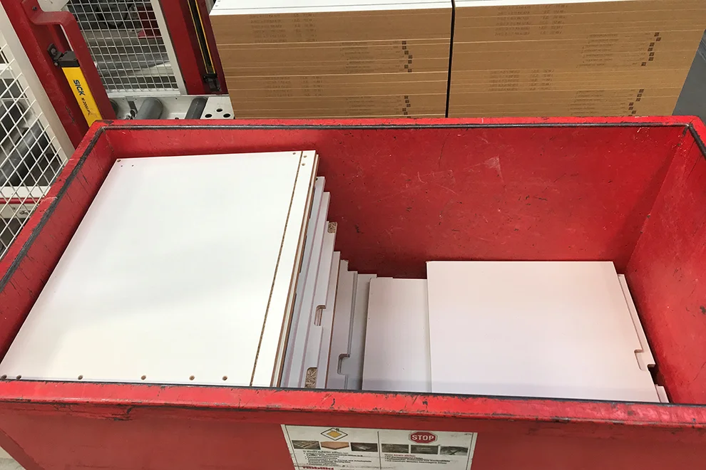 Pile de pièces de mobilier en kit organisées dans une benne métallique rouge prêtes pour l'assemblage ou le transport, vues dans un entrepôt.