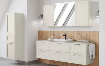 Country-style bathroom furniture in cream with mirror cabinet and wooden back panel.