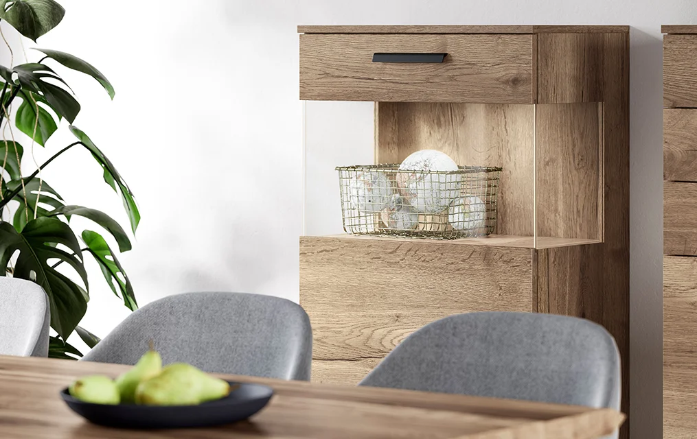 Nowoczesne wnętrze jadalni z eleganckimi szarymi krzesłami, drewnianym kredensem i dekoracyjnymi roślinami, podkreślające minimalistyczny design i naturalne tekstury.